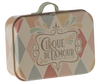 The Maileg Suitcase, Micro is a small rectangular metal box with a handle on top, resembling a mini metal suitcase. It is adorned with a vintage-style pattern featuring pastel-colored triangles and vibrant illustrations. At the center, a label reads "Cirque de l'Amour" in soft shades of pink, green, and cream—ideal for storing small items.