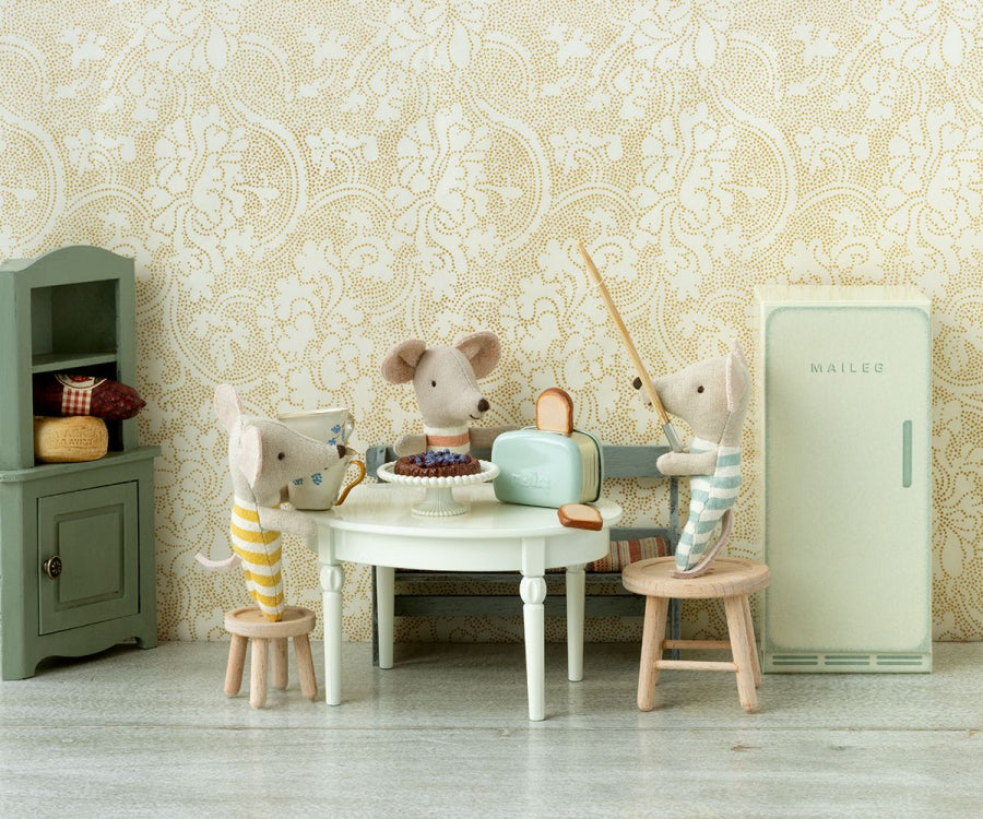 Stuffed mouse family in a cozy kitchen setting with a Maileg | Miniature Toaster - Mint, a cabinet, and a round table with chairs, enjoying toasted bread and tea.