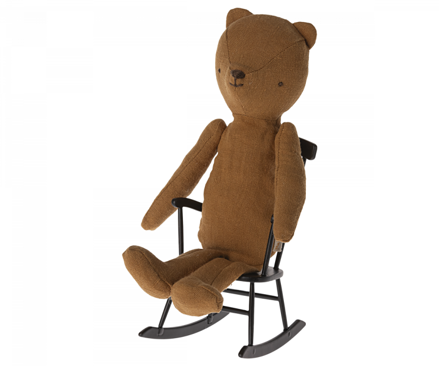 A brown fabric teddy bear with stitched facial features is sitting on a Maileg Rocking Chair, Mini - Anthracite. The teddy bear has a simple, minimalist design with elongated arms and legs, blending seamlessly into the cozy setup of the teddy family furniture.