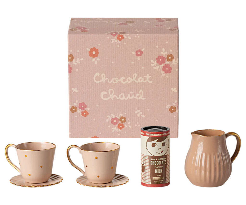 The Maileg Hot Chocolate Set, Mini comes in a beautiful pink gift box adorned with a floral design and the words "Chocolat Chaud." Included in this charming set are two pink mugs with gold polka dots and rims, complete with matching saucers, a brown milk pitcher, and a canister of hot chocolate mix. It's the perfect addition for sharing sweet moments with the Teddy family.