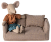 A fabric mouse doll, styled for children, wearing an orange striped shirt and blue skirt rests on a plush Maileg Mouse Couch. The petite couch features a plaid pattern with two cushions, exuding a handmade appeal that captures the Mouse Hole Farmhouse charm.