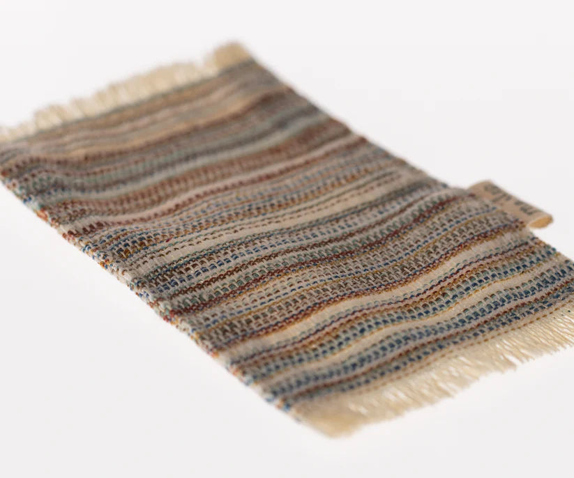 The Maileg Striped Rug, Small features a rectangular piece of fabric with a woven, wavy pattern in earthy tones such as browns, greens, and blues set against a light background. The edges are slightly frayed for added texture, reminiscent of its striped design.