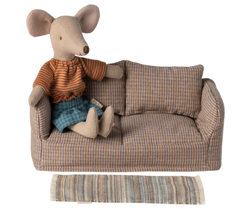 A stuffed mouse toy wearing a striped orange shirt and blue shorts is seated on a plaid-patterned mini sofa with matching cushions. Enhancing the cozy atmosphere, the scene features the Maileg Striped Rug, Large positioned in front of the sofa.