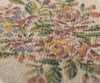 Close-up of the intricately embroidered floral pattern on the Maileg Flower Rug, Medium, showcasing a delicate flower print crafted with an array of green, purple, orange, yellow, and pink threads. The texture of the fabric and stitching is prominently visible.