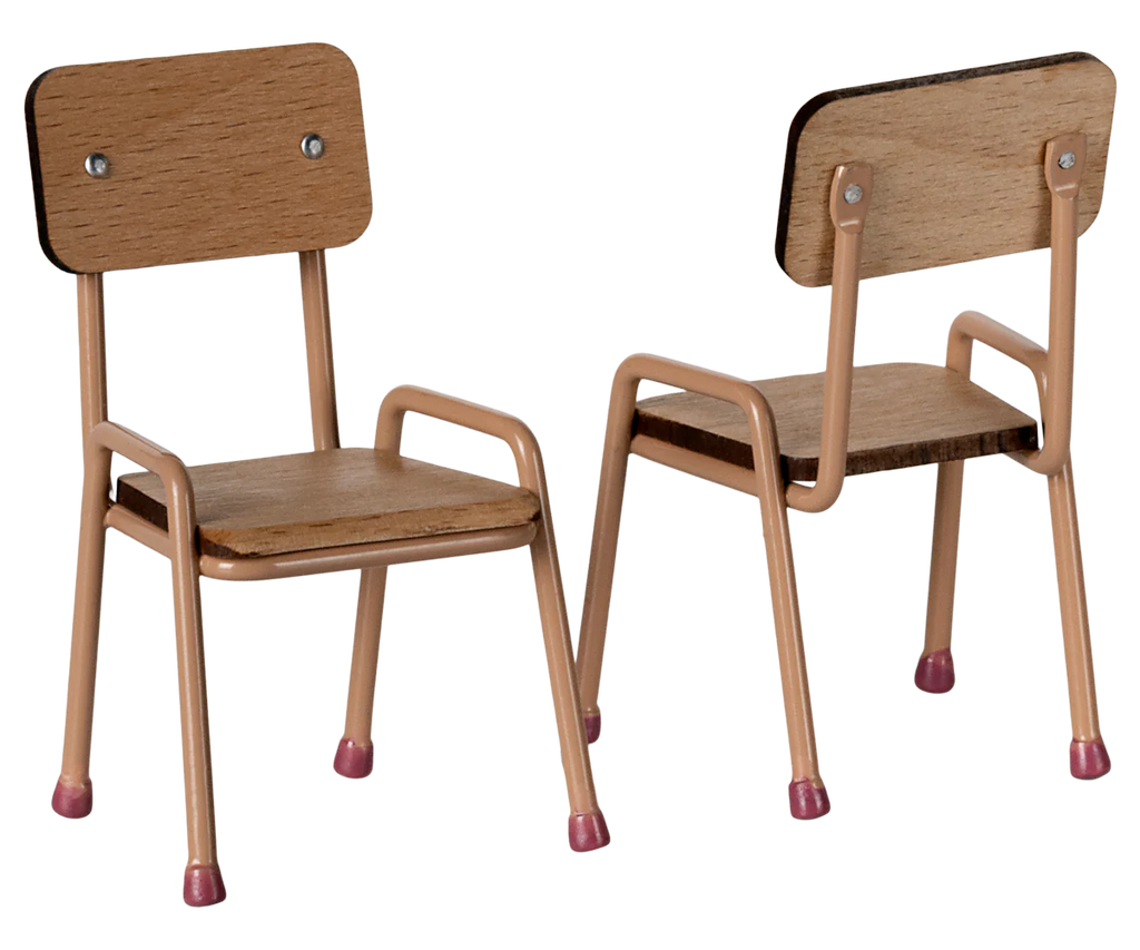 Displayed are two small chairs from the Maileg School Table & Chair Set For Mice in Dark Powder. They feature beech wood with peach metal legs ending in red tips, adding charm with their handmade color details. One chair faces forward, and the other is backward.