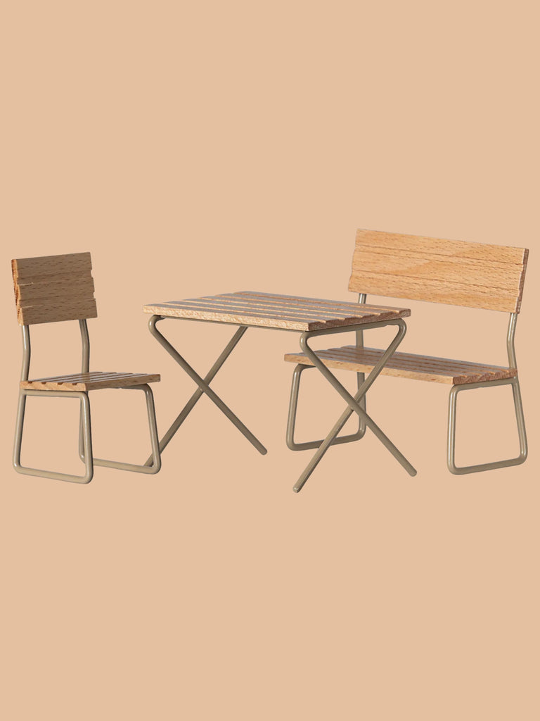 The Maileg Garden Table & Chair Set - Mouse Size features a wooden table, bench, and chair with light wood surfaces and sleek metal frames, creating an inviting outdoor space against a solid beige backdrop. Ships in approximately one week.