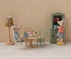 Two toy mice sit at a tiny table with cups and pastries on charming dollhouse furniture. They use the Maileg Vintage Chair, Mouse Size - Dark Powder, creating a cozy scene with dishes and a floral lamp in the background.