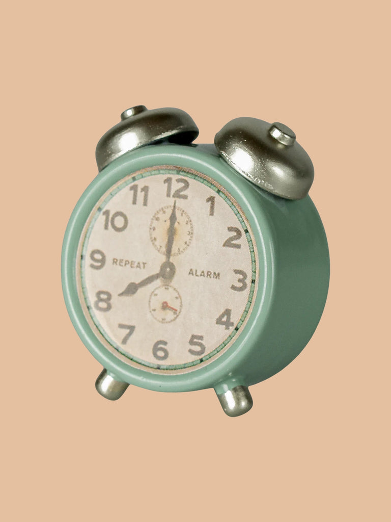 A small, vintage-style Maileg Alarm Clock for Dollhouse in mint with metal silver bells stands against a plain beige background, displaying 10:10 and ready for new adventures. Ships in approximately one week.