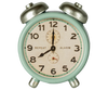 The Maileg Alarm Clock For Dollhouse in mint showcases a vintage style with metal accents, silver bells on top, and a dial marked "REPEAT" and "ALARM." It features black numbers and hands, displaying the time around 10:10. Ships in approximately one week.