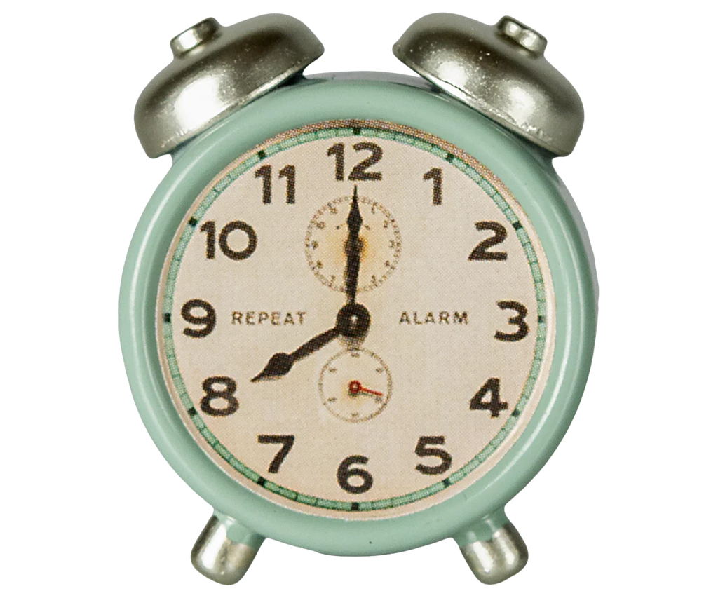 The Maileg Alarm Clock For Dollhouse in mint showcases a vintage style with metal accents, silver bells on top, and a dial marked "REPEAT" and "ALARM." It features black numbers and hands, displaying the time around 10:10. Ships in approximately one week.