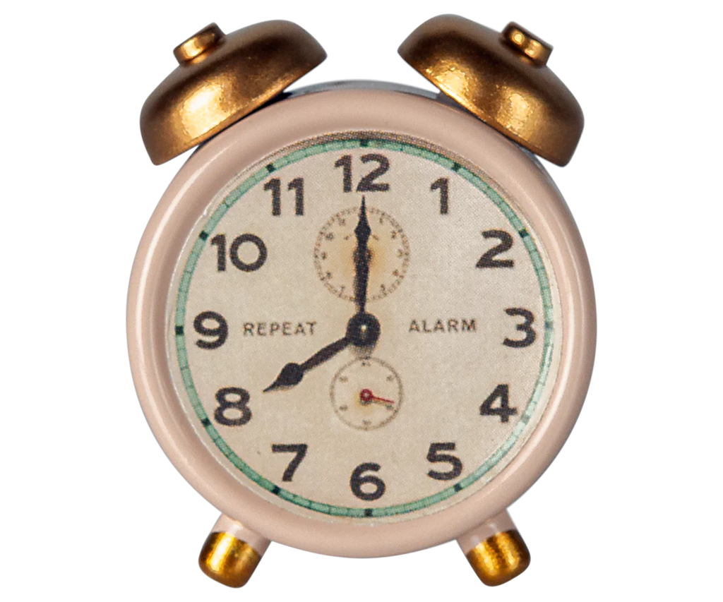 The Maileg Alarm Clock For Dollhouse - Powder, shipping in a week, is a vintage-style pink clock with two brass bells and charming metal accents. Its face shows numbers 1 to 12, small details like repeat and alarm dials, and the hands indicating 10:10.