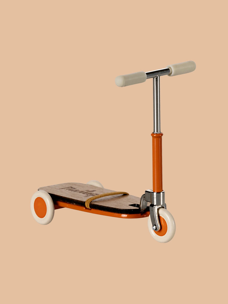 The Maileg Mouse Size Scooter features a vintage-style design with a wooden deck, orange frame, and white wheels set against a solid beige background. It includes wooden details and a T-shaped metal handlebar, shipping in approximately one week.