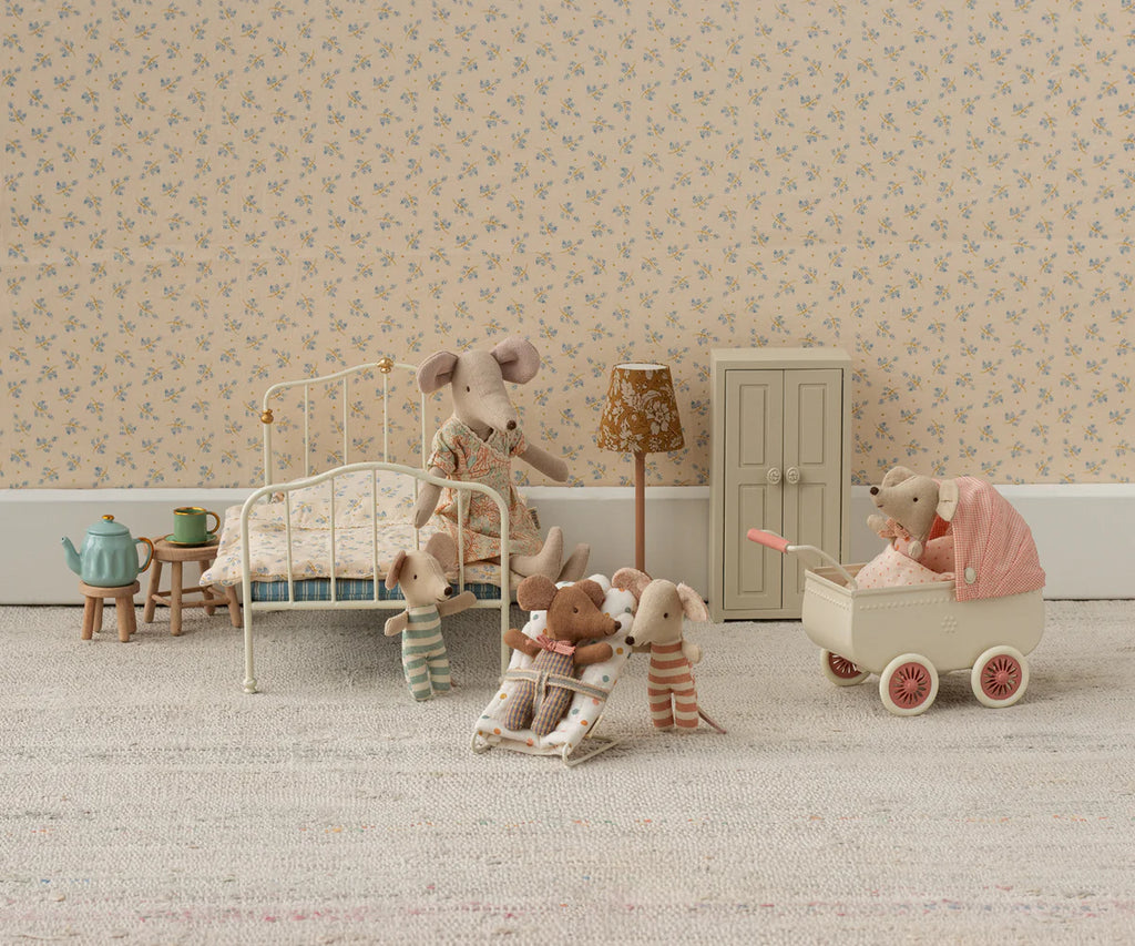 A charming dollhouse scene features mouse dolls in pajamas—some on a soft mattress bed, some with a blanket, and one pushing baby mice in the Maileg Pram, Mouse - Coral. The room has tiny furniture and floral wallpaper.