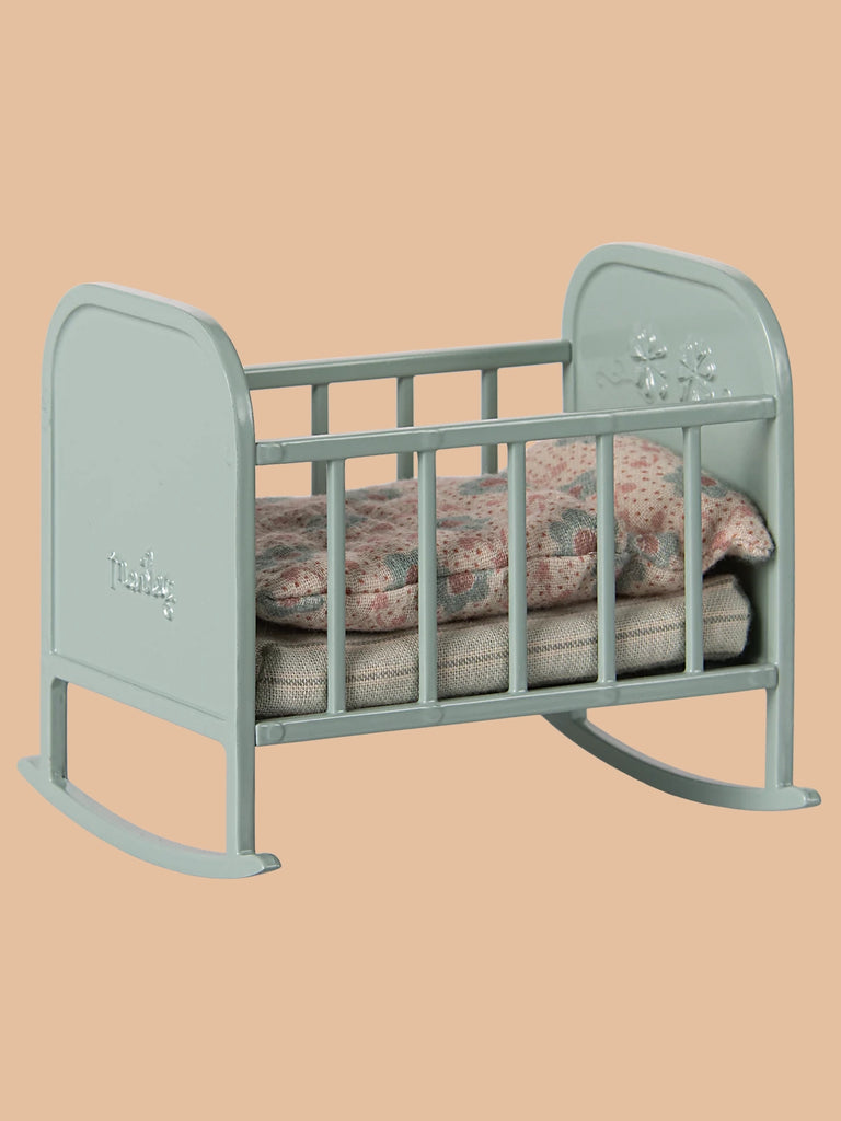 The PRE-ORDER Maileg My Cradle - Blue Mint, available for shipping in late January, features a small design with decorative floral patterns on the headboard, a floral-patterned cushion, and a beige blanket against a light peach background.