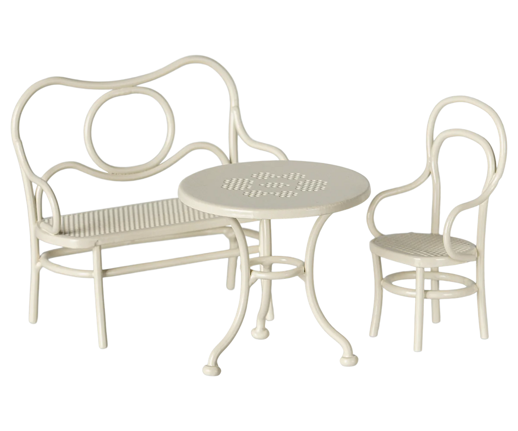 The Maileg Mouse Cafe Set Table & Chair in off-white is a vintage-style set, ideal for dollhouses or miniature furniture. It includes a small round table with a perforated top and two chairs featuring curved ornate designs and matching woven seats. Perfect for creating your own mice café set.