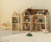 A cozy scene with two wooden dollhouses furnished with miniatures and toy mice, featuring Maileg Wallpaper, Mouse Hole Farmhouse on the walls, plus a toy pig in a stroller and a small green car on a plush white rug in soft light.