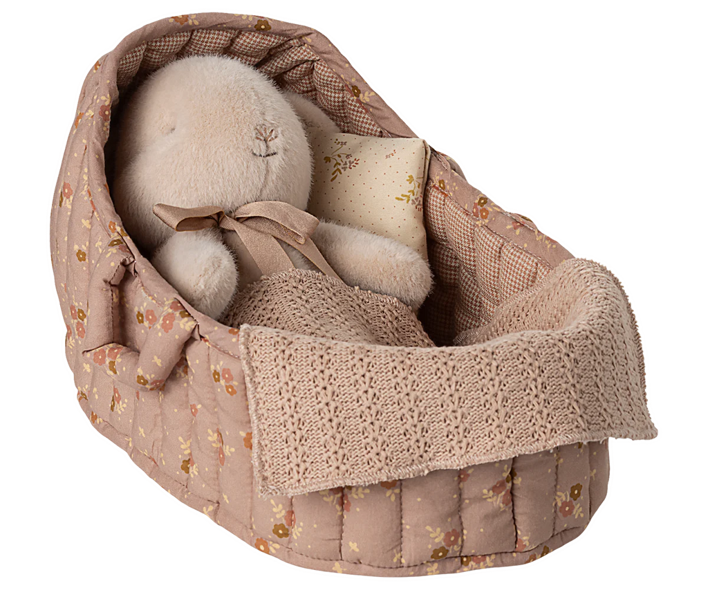 The Maileg Carry Cot, Large - Rose holds a plush toy with a knitted blanket and patterned pillow, creating a cozy, vintage-style setting—perfect for carrying around and comforting your child’s favorite plush friends.