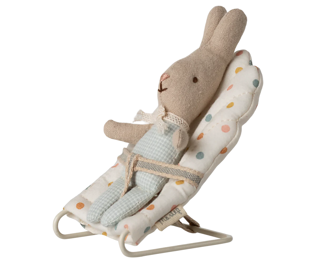 A Maileg My Babysitter - Multi Dots holds a stuffed bunny dressed in blue overalls and a lace collar, secured in its white chair with colorful polka dots and a sturdy metal base.