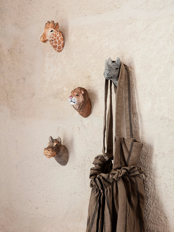 Decorative safari animal head sculptures on a textured wall with a draped fabric hanging off Hand Carved Animal Wall Hooks, featuring designs of a giraffe, lion, rhino, and hippo.