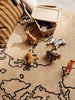 A playful setup of various Hand Carved Wooden Elephants on a sand-colored, map-themed rug with shapes of continents, next to a striped cushion and a small bin with rolled papers.