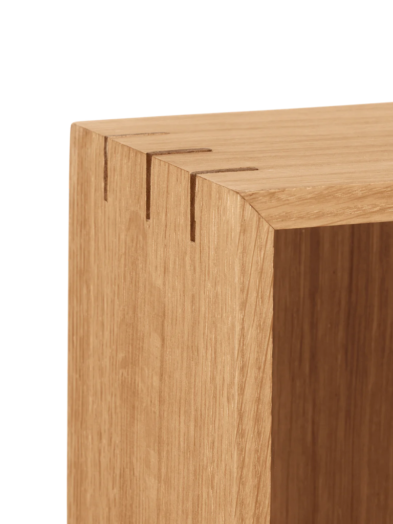 Close-up of a Ferm Living Bon Shelf - Oiled Oak corner showing detailed wood grain and a precise dovetail joint in oiled oak, isolated on a black background.