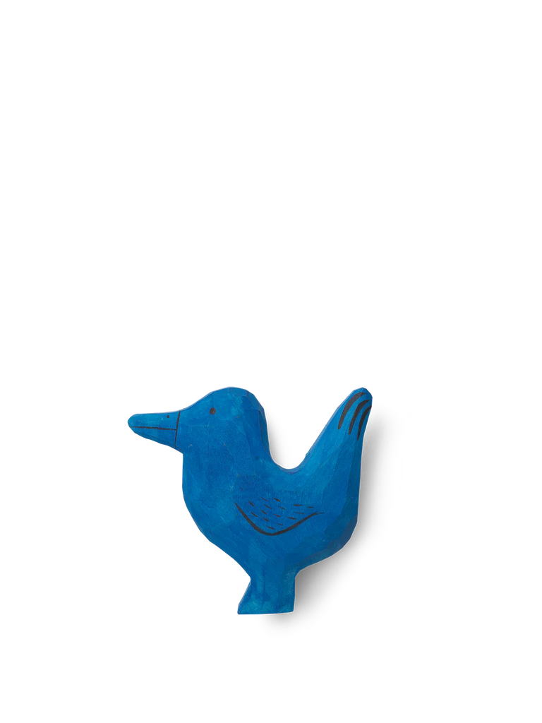 A Ferm Living Hand Carved Wooden Bird Hook, hand-carved from natural materials and painted in bright blue, is displayed against a black background. The bird features a primitive and abstract form, emphasizing.