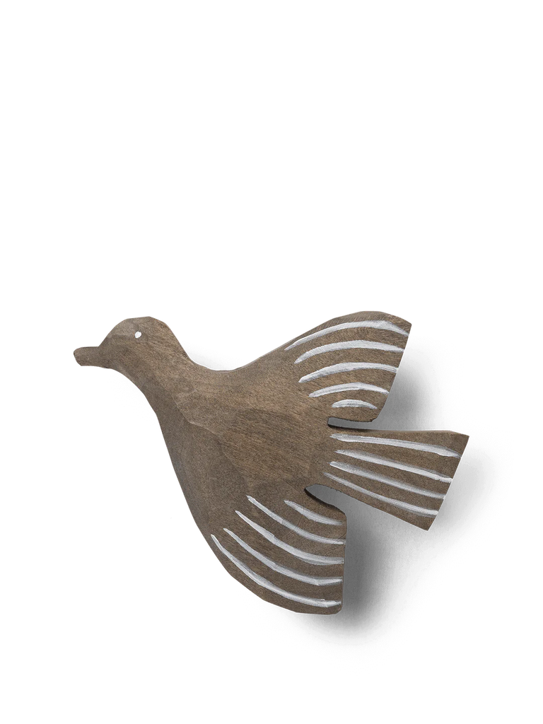A Ferm Living hand-carved wooden bird hook with simplistic design, featuring a dark brown body and stylized white striped wings and tail, isolated against a black background.