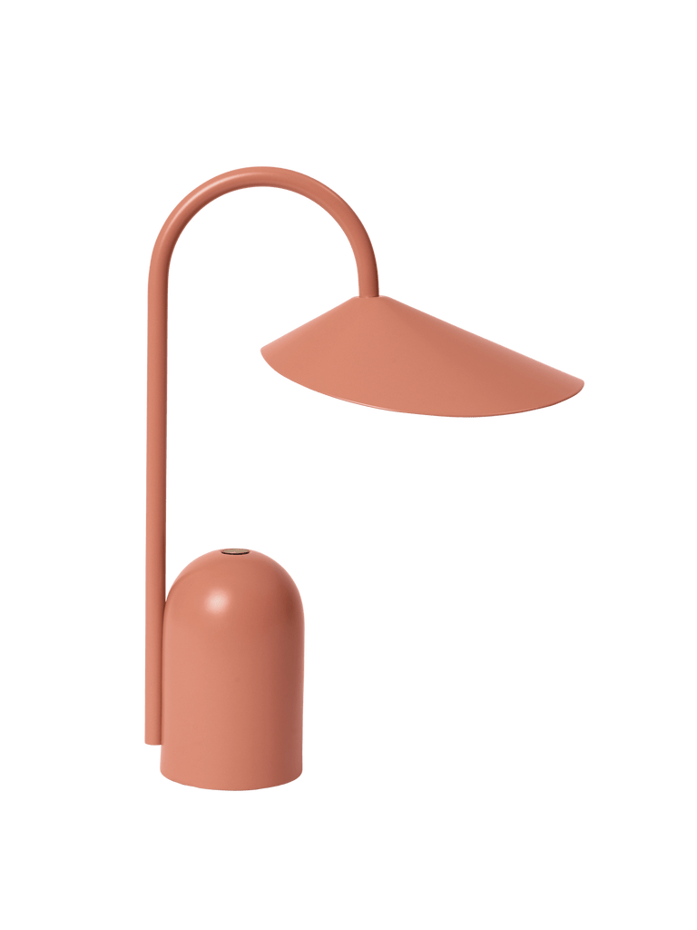The Ferm Living Arum Portable Lamp - Sienna features a modern, minimalist design with a matte terracotta finish, curved stem, and wide slanted shade. This rechargeable LED lamp adds style and function to any space.