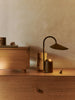 A minimalist wooden sideboard displays the Ferm Living Arum Portable Lamp in Dark Chocolate with touch dimmer, a small cylindrical sculpture, spinning top, and decorative box. Warm lighting adds coziness against a neutral beige wall.