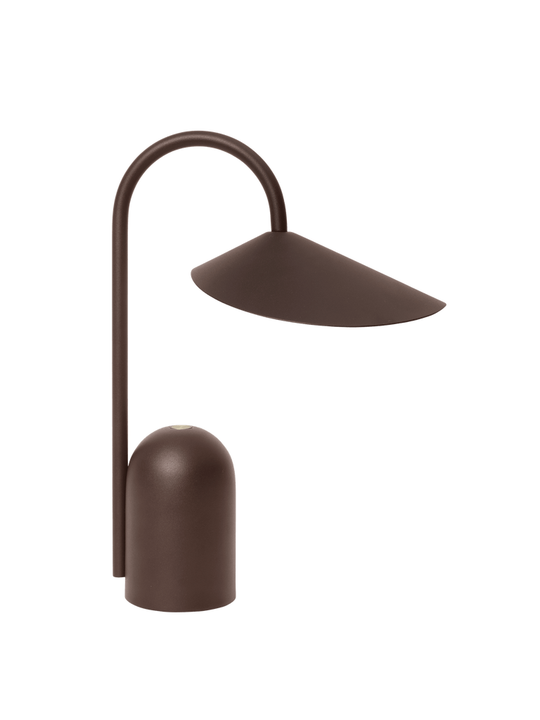 The Ferm Living Arum Portable Lamp in Dark Chocolate features a modern, minimalist design with a curved stand and an angled, wide lampshade, shown against a plain white background.