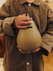 A child in a brown shirt holds the Ferm Living Pear Money Bank with both hands, one on the stem and one at the base—a charming piece for children's room decor.