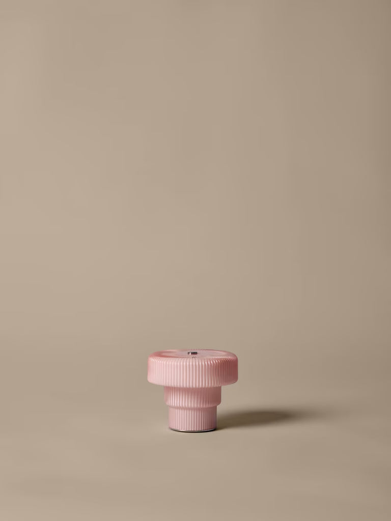 The Ferm Living Ripple Portable Lamp in Pale Rose sits centered on a plain beige background, its gentle, dimmable LED glow casting a soft shadow to the right.