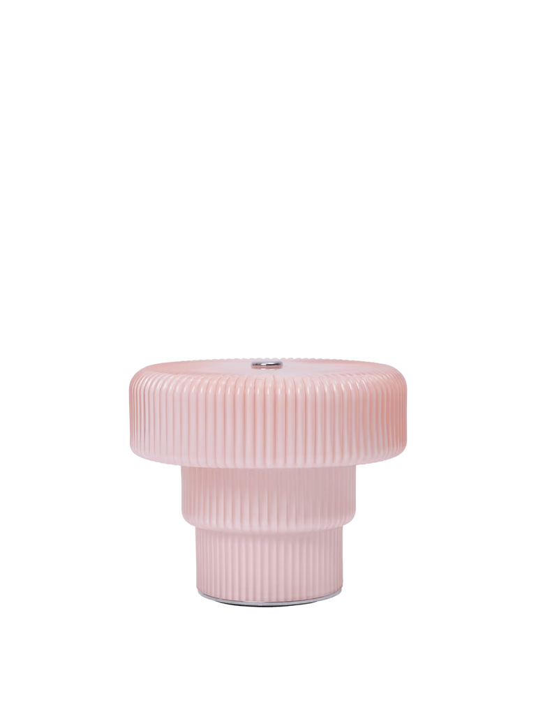 The Ferm Living Ripple Portable Lamp in Pale Rose is a modern, pink table lamp with a ribbed, mouth-blown glass design and a wide, rounded top on a cylindrical base, shown against a plain white background.