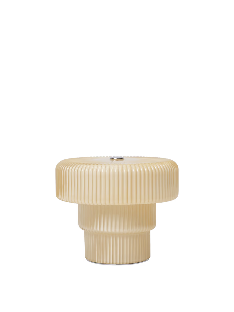 The Ferm Living Ripple Portable Lamp - Oat is a cream-colored, ribbed cylindrical lamp with a wide flat top, a narrower base, mouth-blown glass construction, dimmable LED light, and is shown against a plain white background.