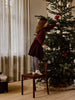 A young girl stands on a chair to hang a silver Ferm Living Holly Leaf Ornaments - Set of 4 - Silver on a Christmas tree.
