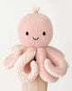 A hand holds the Cuddle + Kind Baby Octopus (Soft Coral Pink), an heirloom-quality, hand-knit plush toy with a smiling face, black eyes, and light pink tentacles, crafted from soft Peruvian cotton yarn against a white background.