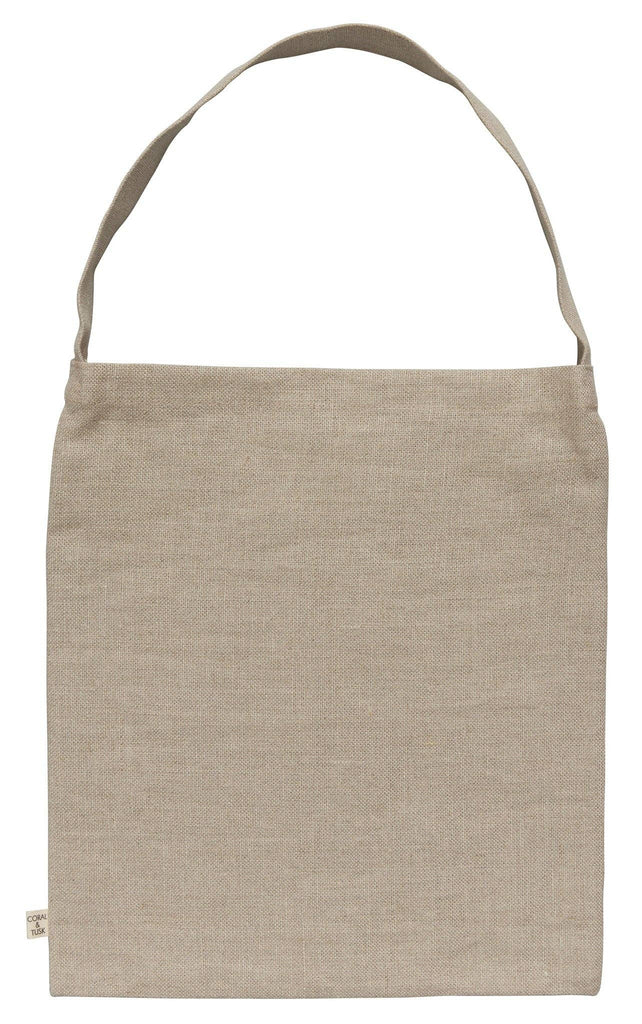 The "Dogs and Toys Tote" is a light brown linen tote bag with a textured appearance, featuring a dog theme. It has a long strap and a small side tag for branding, offering a charming minimalist look.