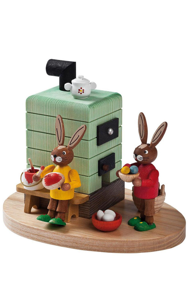 Decorative figurine made in Germany, featuring the Collectible Richard Glaesser Incense Burner - Rabbits At Stove at a wooden painting station with a large green camera-shaped structure and scattered paint pots. One rabbit holds a palette; the other paints. A small