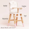 The Dolls Wooden High Chair is a small, eco-friendly wood chair featuring a white seat, scallop backrest, feeding tray, decorative legs with pink tips, and footrest. Perfect for pretend play. Text: "Hand Made with Love.
