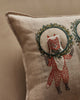 The Christmas Wreath Trio Pocket Pillow is a beige accent pillow with detailed stitching, featuring a red fox standing upright and holding a circular green holiday wreath—perfect for adding woodland charm to your space.