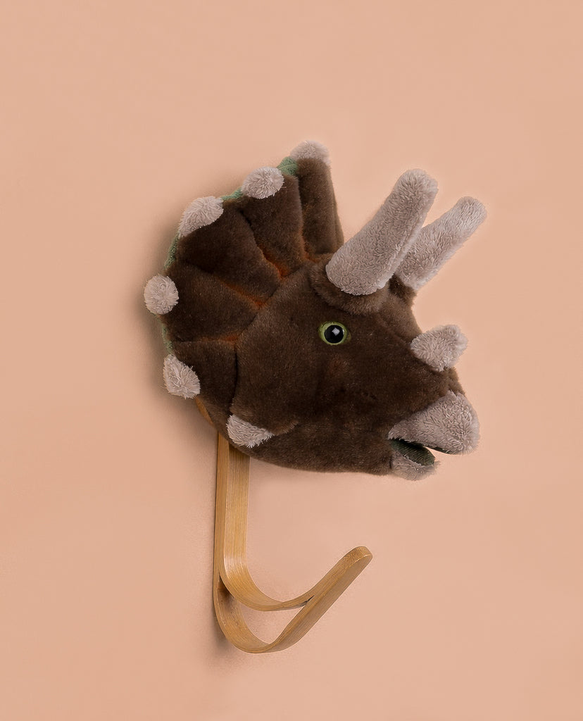 The Coat Hanger - Triceratops Dino is a wall-mounted, light wood hook with a plush brown and gray triceratops head, shown against a plain beige background.