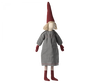 A Maileg Christmas Small Pixy with a red pointed hat, blond yarn hair, and a gray cotton dress stands upright. The pixy has dark red shoes and striped stockings.