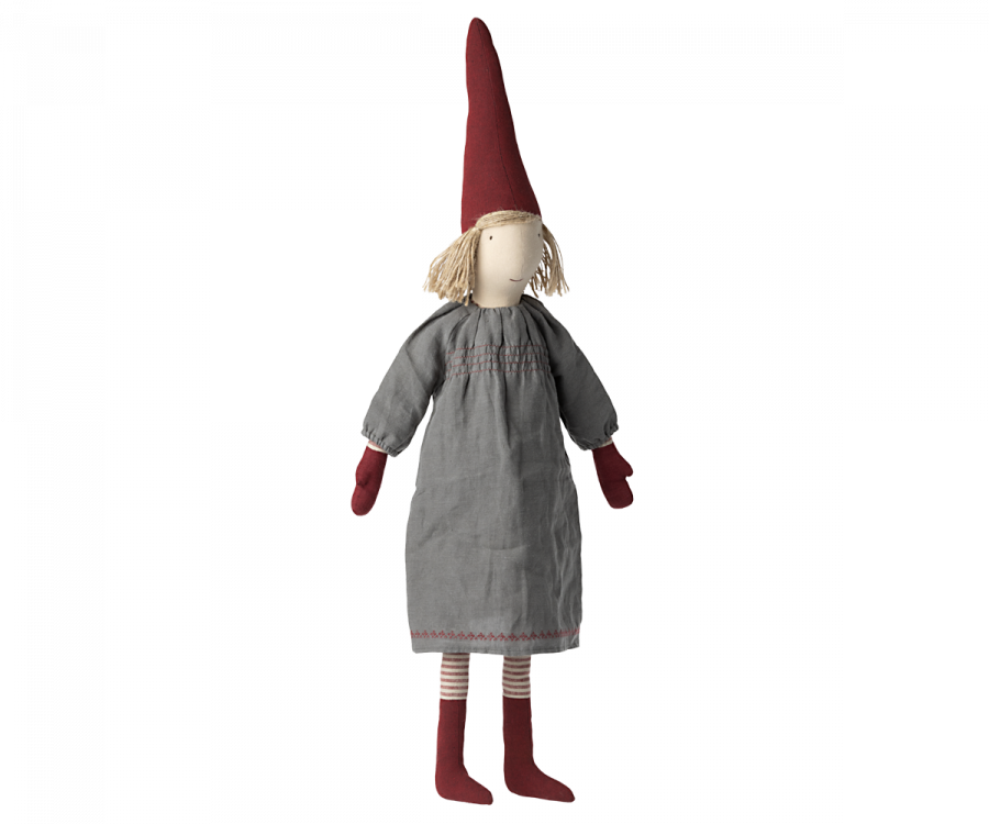 A Maileg Christmas Small Pixy with a red pointed hat, blond yarn hair, and a gray cotton dress stands upright. The pixy has dark red shoes and striped stockings.