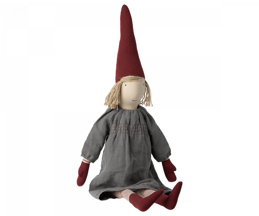 A Maileg Christmas Small Pixy doll with a long red pointed pixy hat, blonde yarn hair, and a grey dress sitting against a plain background. The doll has striped red and white legs and simple features.