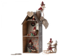 A decorative Christmas-themed Maileg Cardboard Two-Story Gingerbread House with three levels featuring festive dolls and ornaments such as a wreath, gingerman, and a gnome. A sled rests outside the house, set against