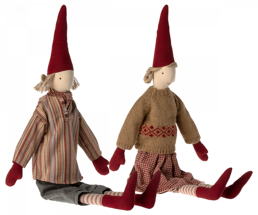 Two Maileg Christmas Pixy (Size 4) dolls, one in a striped shirt and grey pants, the other in a brown sweater and plaid pants, sitting with legs stretched out as Christmas decorations, isolated on a black background.