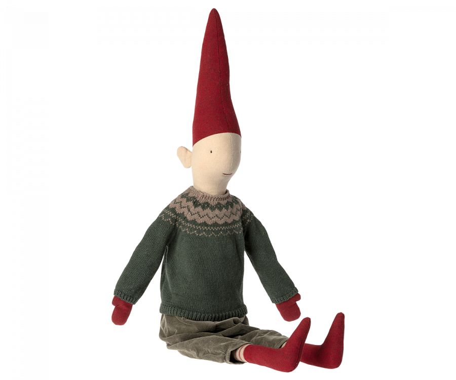 A Maileg Christmas Pixy (Size 5) with a pointed red hat, green sweater, brown pants, and red shoes, seated on an invisible surface against a black background, designed as an exclusive Christmas decoration.