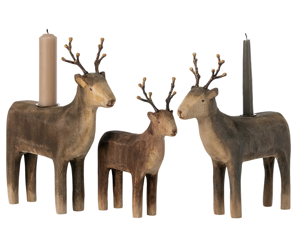 Three Maileg Wooden Reindeer Candle Holders and two candles on a neutral background. The deer, varying in size, depict a family scene with ornate antler details and are sold separately.