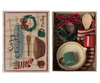 The Maileg Cosy Christmas Set is a delightful gift box featuring charming Christmas accessories, including a wooden spoon, woven fabric, and a decorative wreath adorned with a red ribbon. Inside the box, you'll find a green mug and a red mug. The lid is beautifully illustrated with mugs and wreaths, accompanied by the cheerful text "Cozy Christmas" in a festive design.