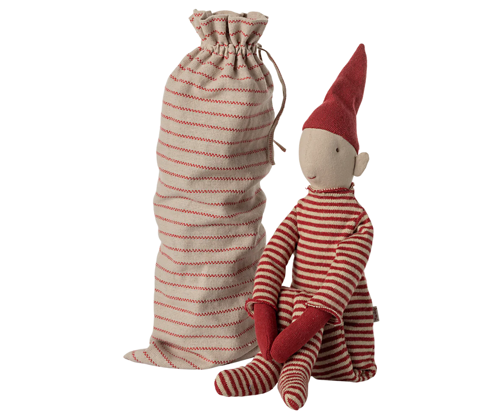 The Maileg Long Legged Pixy, Large, dressed in red and white striped clothing with a pointy hat, sits beside its matching striped drawstring bag. This whimsical creature with pointed ears adds a touch of magic to your decor.